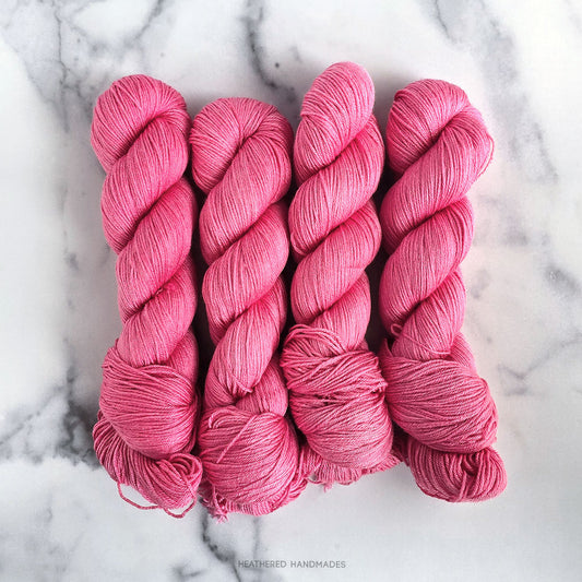 Four pink skeins of yarn on a marble surface with 'Heathered Handmades' branding.
